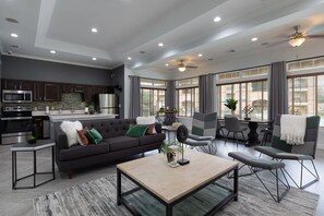 A modern living room with a dark sofa, a coffee table, and a dining area with chairs and a table. - Landing | Beautiful 1BD, Gym (McKinney)