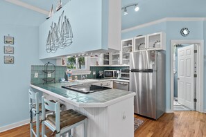A kitchen with a central island, white cabinetry, stainless steel appliances, and a blue wall. - Lulé Cottage (Destin)