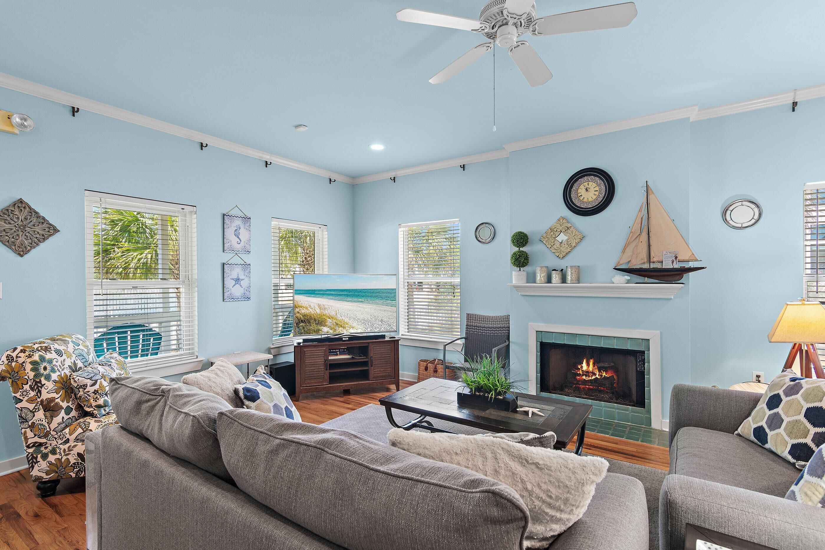 A living room with a fireplace, a ceiling fan, and a view of the beach through the windows.
