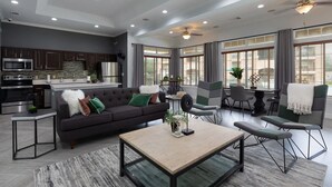 A modern living room with a dark sofa, a coffee table, and a dining area with chairs and a table. - Landing | Incredible 1BD, Gym (McKinney)