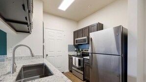 A kitchen with stainless steel appliances, a granite countertop, and a white door. - Landing | Incredible 1BD, Gym (McKinney)