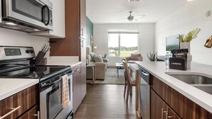 Een moderne keuken met een magnetron, fornuis en een gootsteen. Er is een zithoek met een bank en uitzicht op de omgeving.