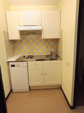 Cocina compacta con alacenas blancas, lavavajillas, estufa y salpicadero de azulejos.