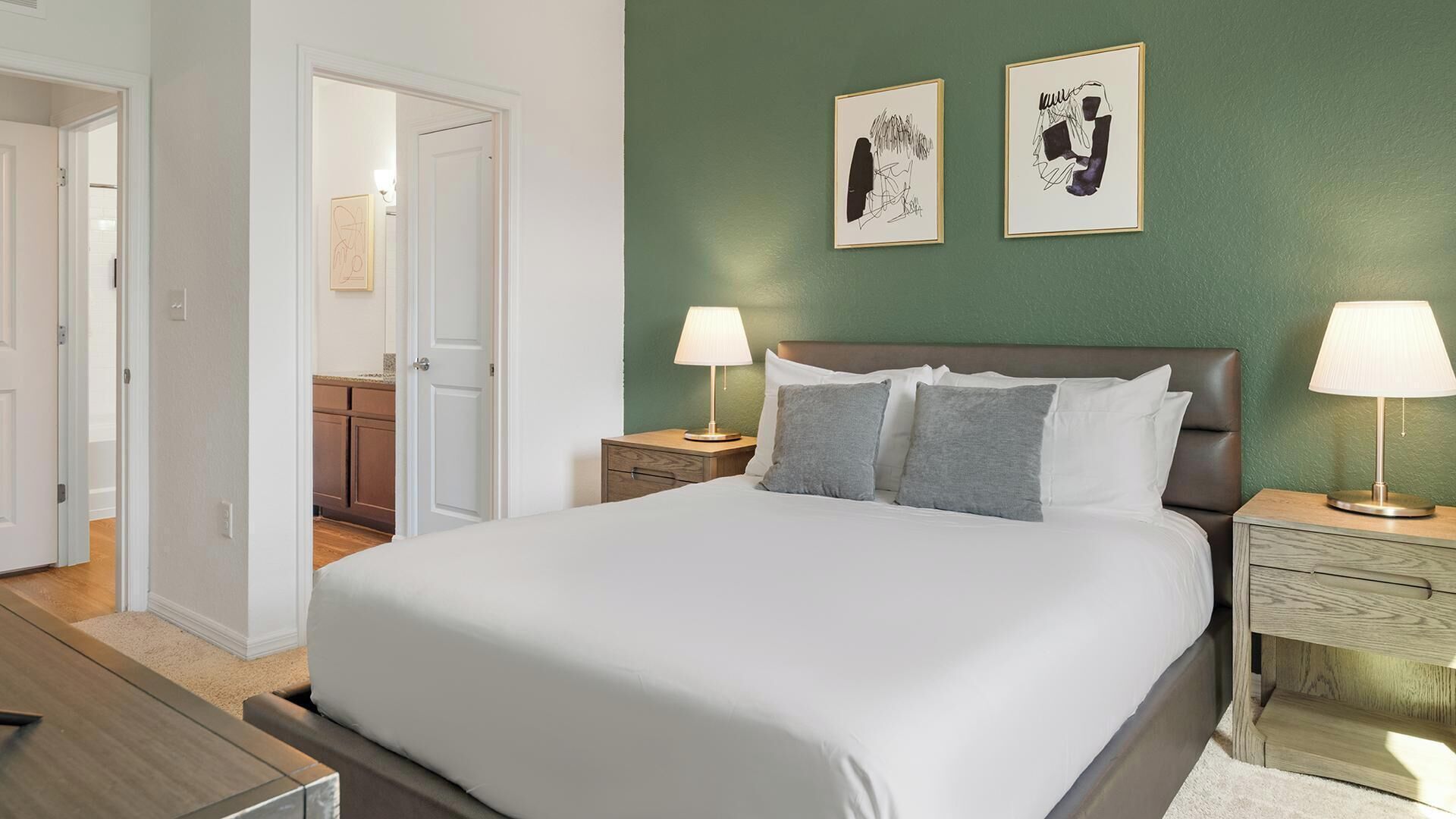 A hotel room with a large bed, two bedside tables with lamps, a green accent wall, and two framed artworks.