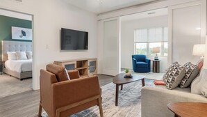 Ein modernes Wohnzimmer mit Sofa, Ohrensessel, Couchtisch und einem wandmontierten Flachbildfernseher.