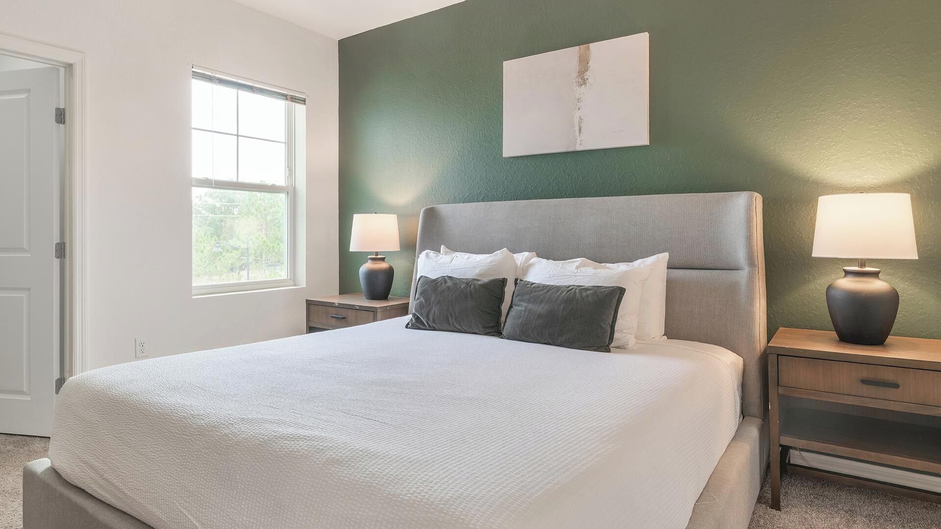 A bedroom with a bed, two bedside tables, a window, and a wall-mounted artwork.