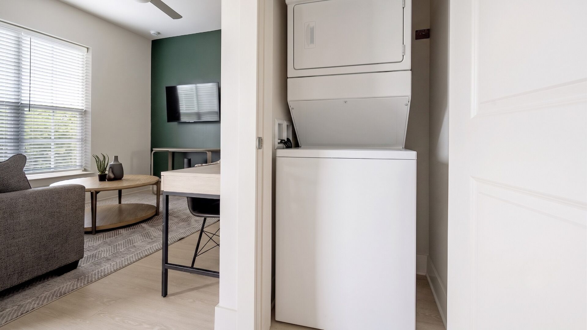 Un espace de vie compact comprenant un canapé, une petite table, un téléviseur et un appareil électroménager blanc, vraisemblablement un lave-linge et un sèche-linge, situés dans un couloir.