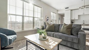 A modern living room with a grey sofa, a blue armchair, and a wooden coffee table with a plant. - Landing | Stylish 2BD, Game Room, Gym (Charlotte)