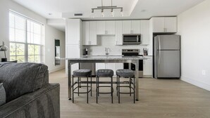 Una cocina moderna con gabinetes blancos, electrodomésticos de acero inoxidable, una encimera de granito y una zona con taburetes de bar.