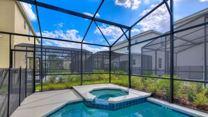 A swimming pool with a hot tub, surrounded by a glass enclosure with a view of a residential area.