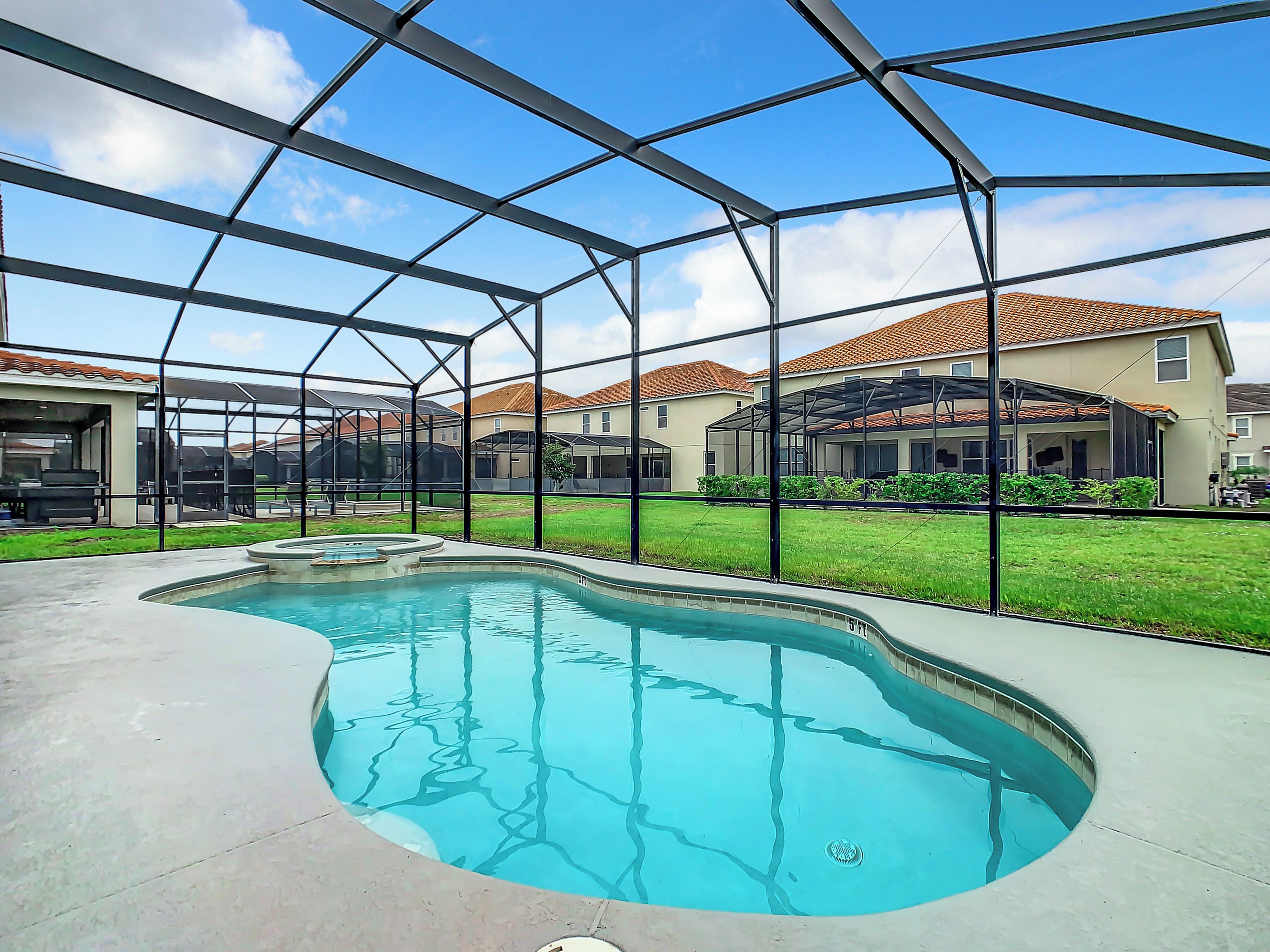 A swimming pool with a curved design, surrounded by a metal fence, and houses in the background.