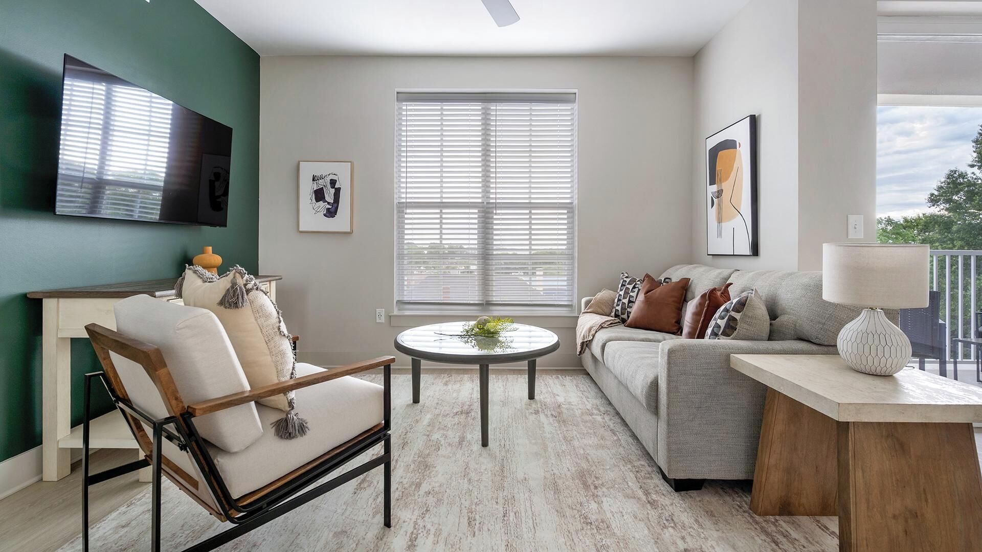 A living room with a sofa, armchair, coffee table, and a TV mounted on the wall.