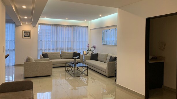 A modern living room with a sectional sofa, a glass coffee table, and a view of the city through large windows. - Apartment in central area for world cup (Naucalpan de Juárez)