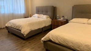 A hotel room with two beds, a wooden floor, a nightstand with a lamp, and a window with curtains. - Apartment in central area for world cup (Naucalpan de Juárez)