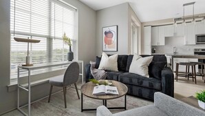 Un salon moderne avec un canapé gris, une table basse et un coin repas, la cuisine étant visible au fond.