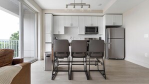 A modern kitchen with white cabinets, a stainless steel refrigerator, a microwave, and a dining area with three chairs. - Landing | Amazing 1BD, Gym, Game Room (Charlotte)