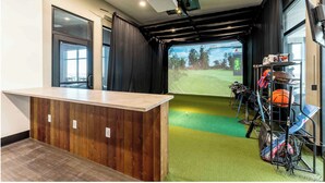 Ein Zimmer mit einem Holzbüro, einem großen Bildschirm, der einen Golfplatz zeigt, und einem Gestell für Sportgeräte.