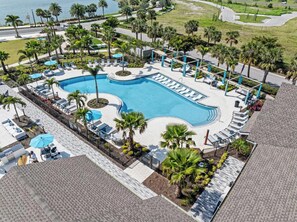 A large swimming pool with sun loungers and palm trees, surrounded by a paved area and a view of the ocean. - Landing | Spectacular 1BD, Clubhouse, Gym (Laurel)