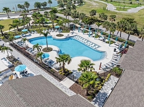 A large swimming pool with sun loungers and palm trees, surrounded by a paved area and a view of the ocean. - Landing | Spectacular 1BD, Gym, Clubhouse (Laurel)