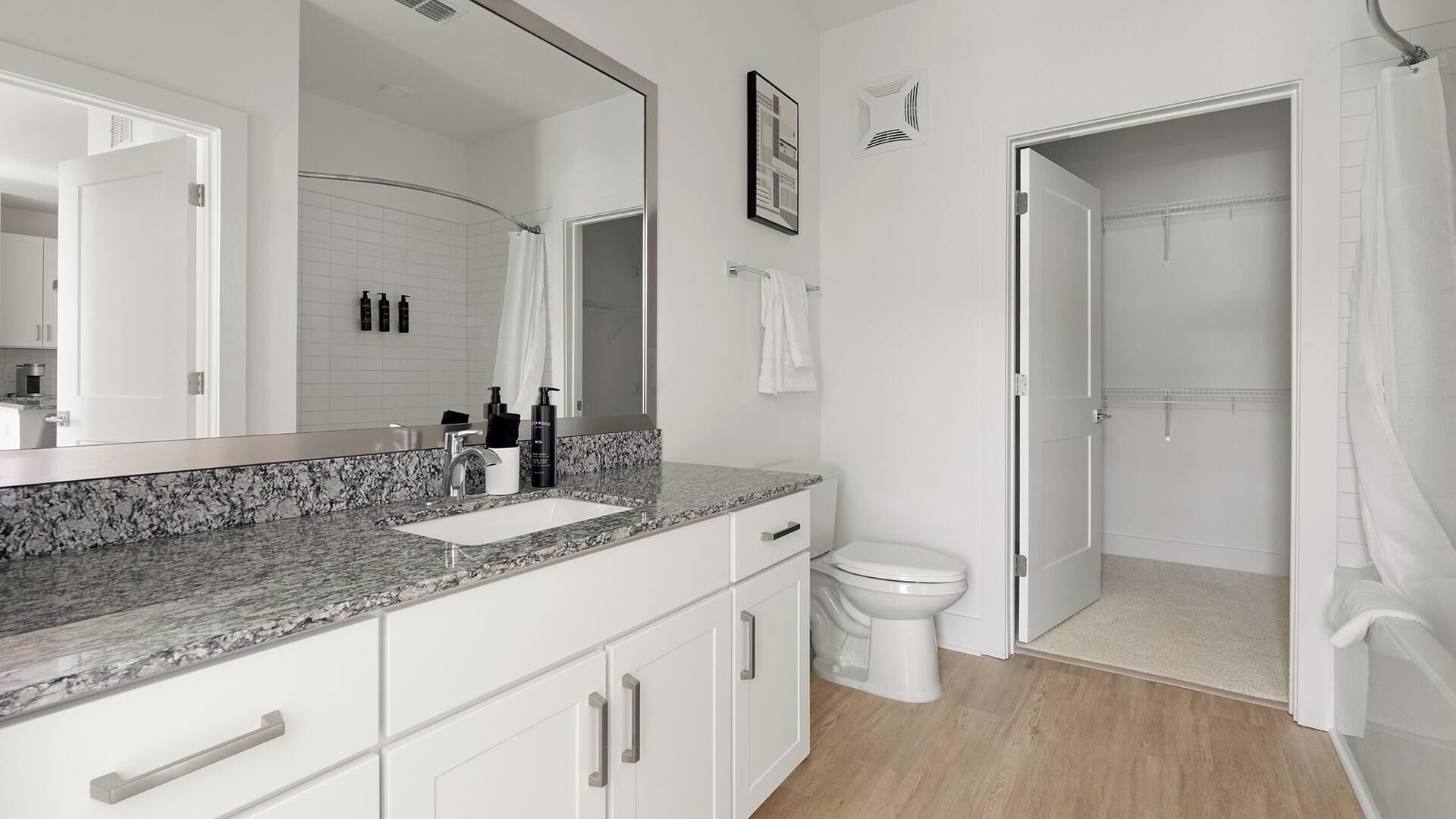 Ein modernes Badezimmer mit Marmorplatte, einem großen Spiegel, einer Toilette und einem Duschbereich.