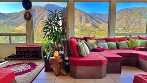 Ein Wohnzimmer mit einem großen Fenster, einem roten Sofa, einem Holztisch und einer Zimmerpflanze.