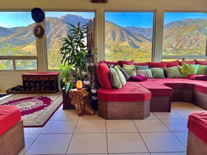 Ein Wohnzimmer mit einem großen Fenster, einem roten Sofa, einem Holztisch und einer Zimmerpflanze.