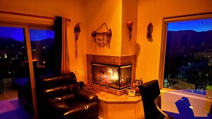 Ein Wohnzimmer mit Kamin, einer schwarzen Ledersofa, einem Esstisch und Blick auf die nächtliche Stadt.
