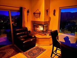 Ein Wohnzimmer mit Kamin, einer schwarzen Ledersofa, einem Esstisch und Blick auf die nächtliche Stadt.