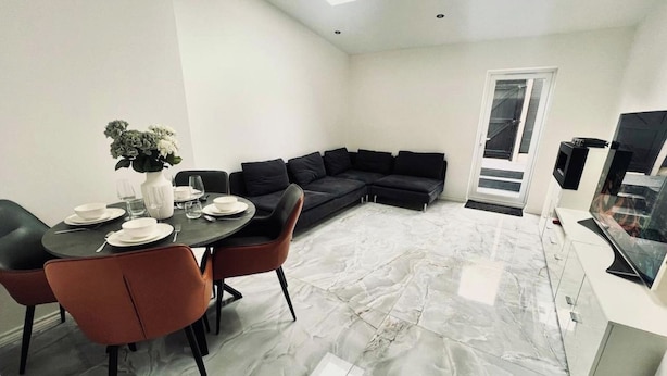 Una sala de estar moderna con comedor, un sofá negro y un televisor de pantalla plana.