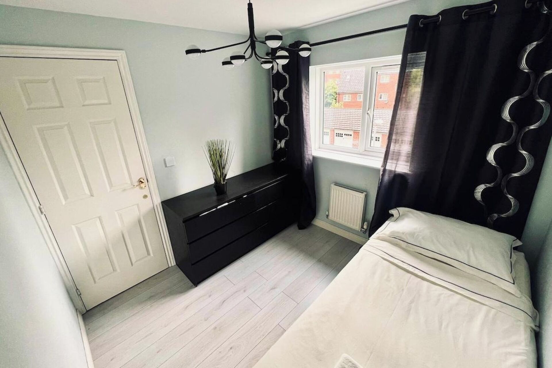 A bedroom with a bed, a dresser, a radiator, a window, and a door.