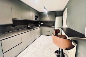 A modern kitchen with grey cabinets, a black countertop, and a bar area with a stool.