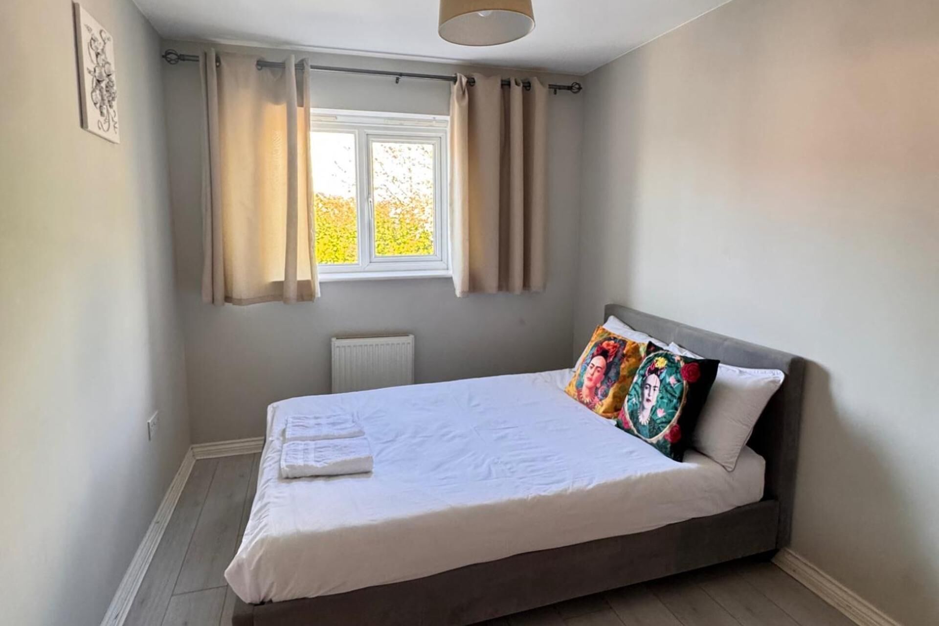Une chambre à coucher avec un lit, une fenêtre avec des rideaux, un radiateur et un tableau accroché au mur.