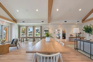 A spacious dining area with a long wooden table, white chairs, and a potted plant. - Landing | Chic 2BD, Gym, Clubhouse (Laurel)