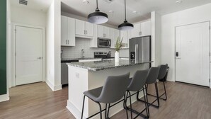 Une cuisine moderne avec des meubles blancs, un plan de travail en granit, un réfrigérateur en acier inoxydable et un îlot central doté de tabourets de bar.