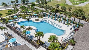 Une grande piscine entourée de chaises longues et de palmiers, avec une zone dallée et une vue sur l’océan.