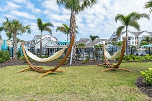 Ein Resort mit zwei Hängematten in einer grünen Rasenfläche, Palmen und einem Pool im Hintergrund.