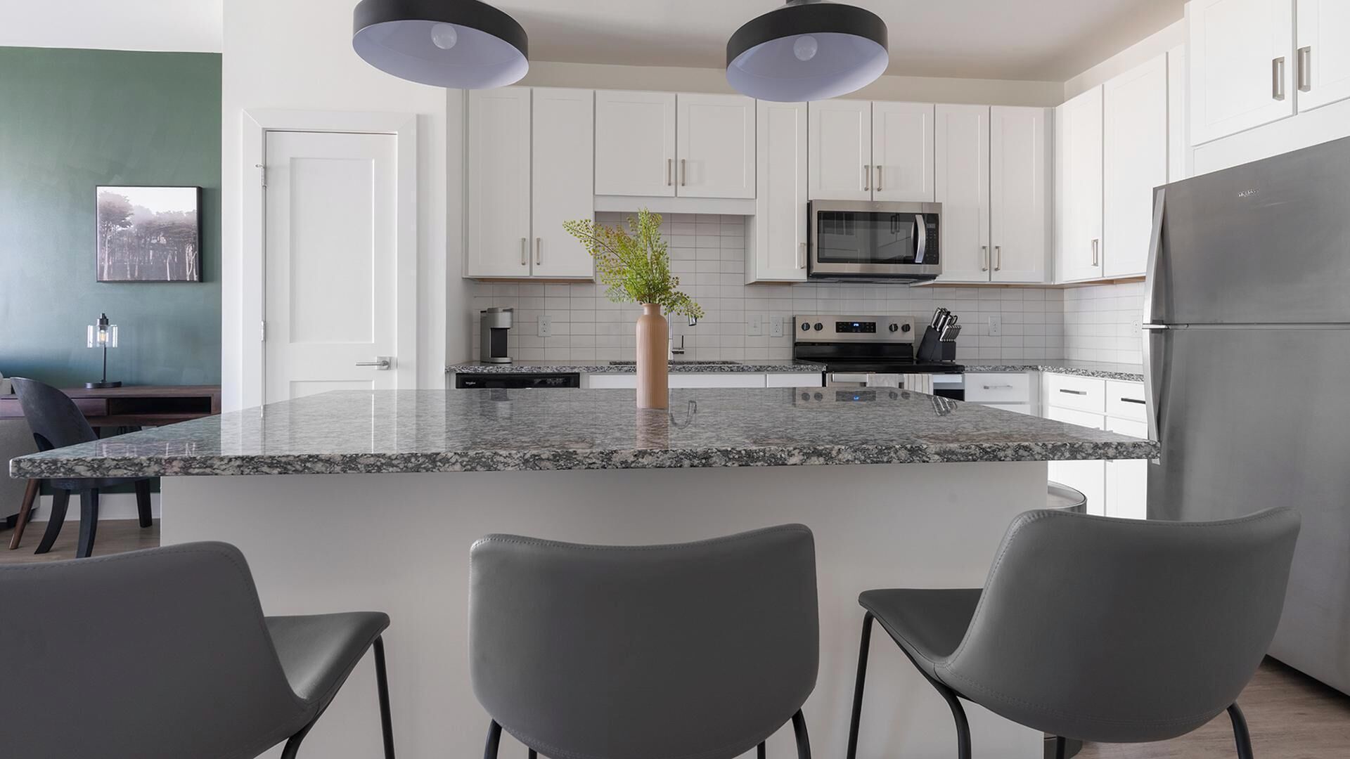 A modern kitchen with white cabinets, a granite island, and a stainless steel refrigerator.
