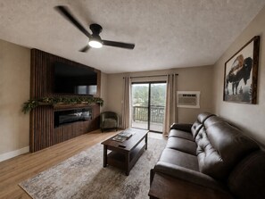 Una sala de estar con televisor, chimenea, sofá de cuero y ventilador de techo.
