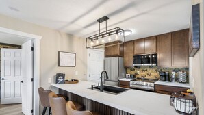 A kitchen with a marble countertop, wooden cabinets, a built-in stove, and a hanging light fixture.