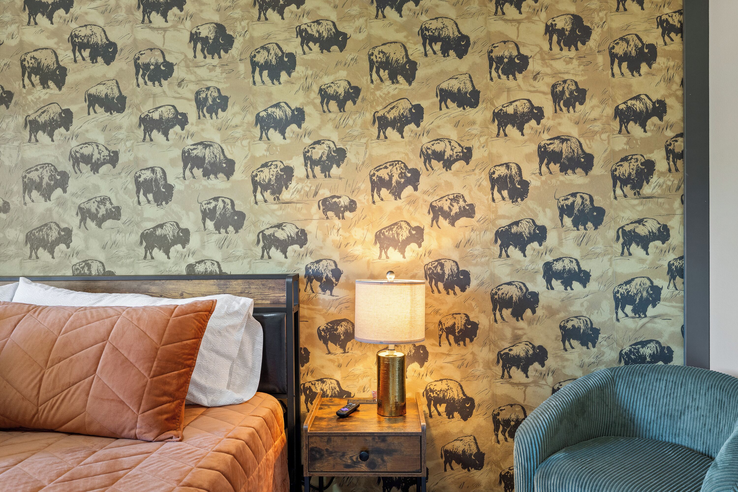 Une chambre avec un lit, une table de chevet avec une lampe et un mur orné d’un motif représentant des buffles.