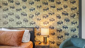 Une chambre avec un lit, une table de chevet avec une lampe et un mur orné d’un motif représentant des buffles.