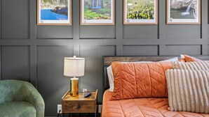 A bedroom with a bed, a nightstand with a lamp, a chair, and four framed pictures on the wall.