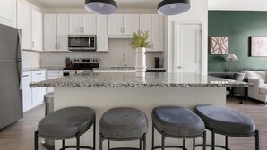 Una cocina moderna con gabinetes blancos, encimera de granito, microondas integrado y una isla grande con taburetes de bar.