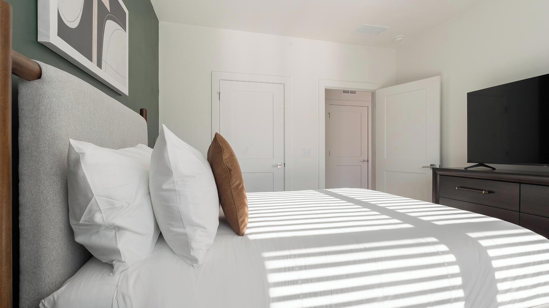 A bedroom with a bed, pillows, a TV, and two doors.