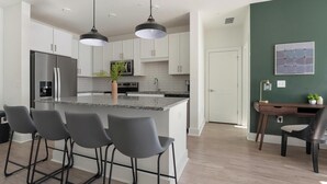 Une cuisine moderne avec des meubles blancs, un îlot central doté de tabourets, un réfrigérateur et un four à micro-ondes.