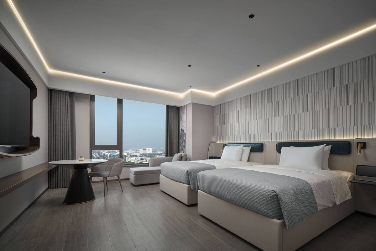 A modern hotel room with a large bed, a desk, and a view of the city.
