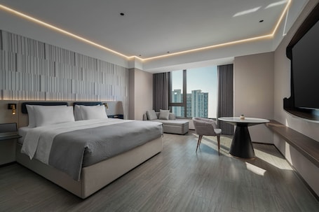 A modern hotel room with a large bed, a small sofa, a round table, and a TV mounted on the wall.. Wanda Moments Changzhou Intl. Airport