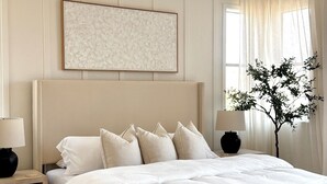 Ein Schlafzimmer mit einem Bett, Nachttischen, einer Bank, einem Deckenventilator, einem Fenster mit Vorhängen und einem Wandbild.