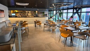 Interior moderno de restaurante com área de bar, disposição de assentos e grandes janelas.