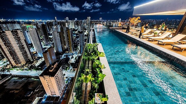 Piscina no terraço com vista para a cidade, rodeada por edifícios altos.